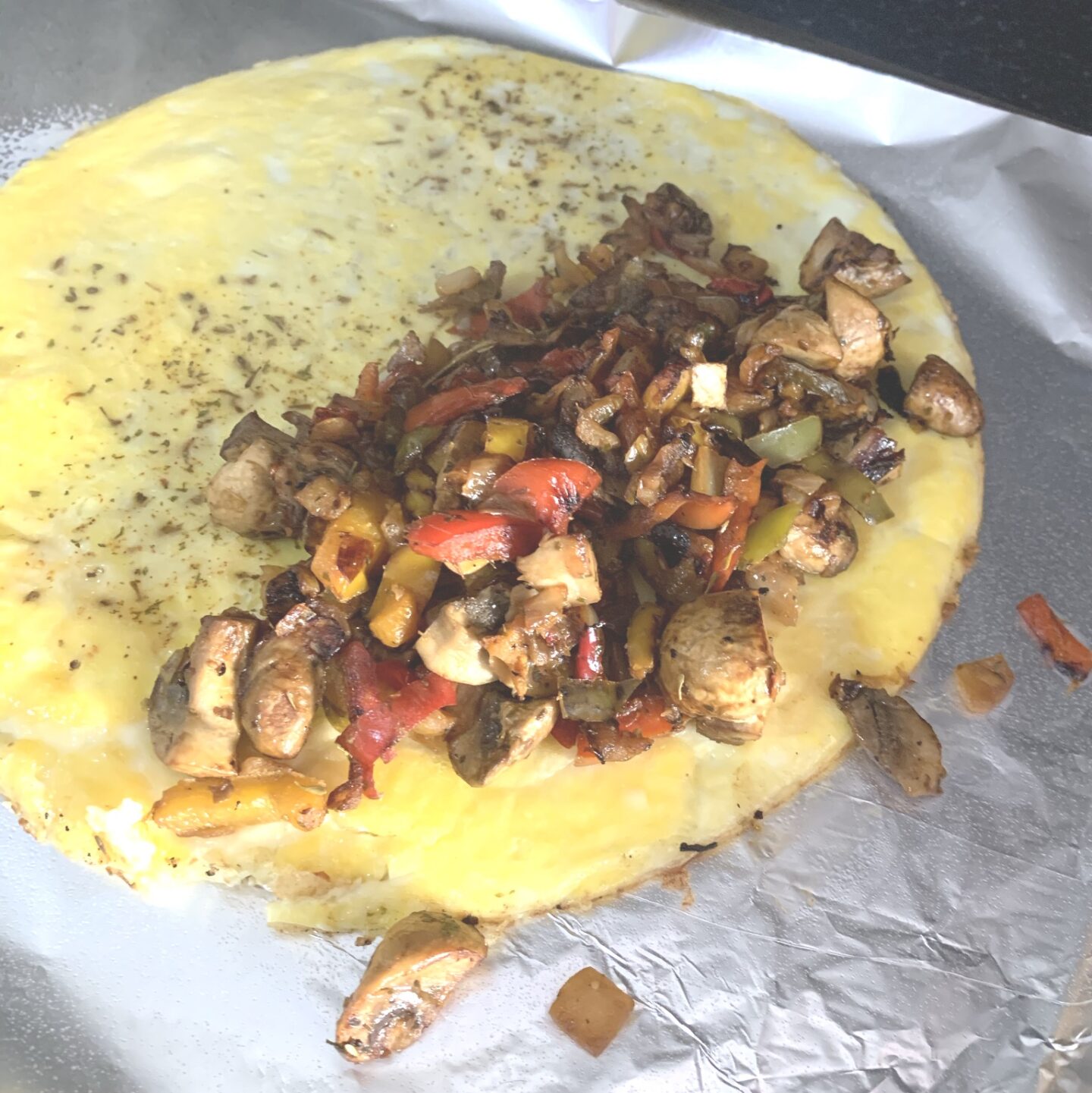 an omelette laid flat with half of it filled with cooked vegetables